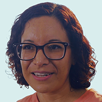 Woman smiling broadly outdoors with greenery.