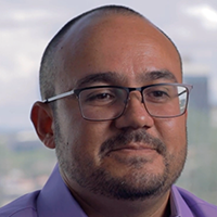 Woman wearing hat and sunglasses outdoors in the snow, looking at the camera.