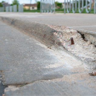 Broken sidewalk curb with exposed rebar and jagged edges