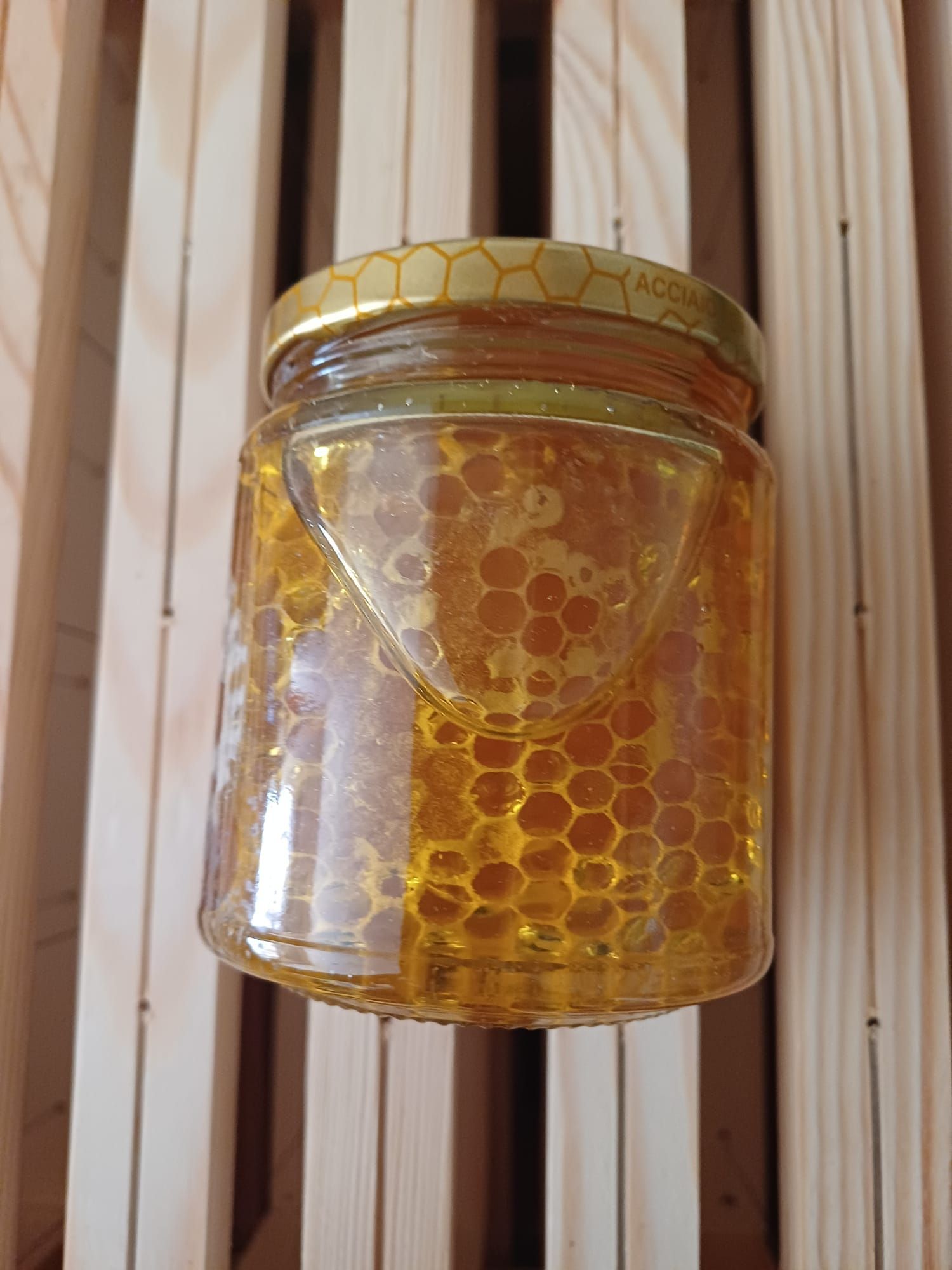 Barattolo di miele con favo all'interno, su una superficie di legno.