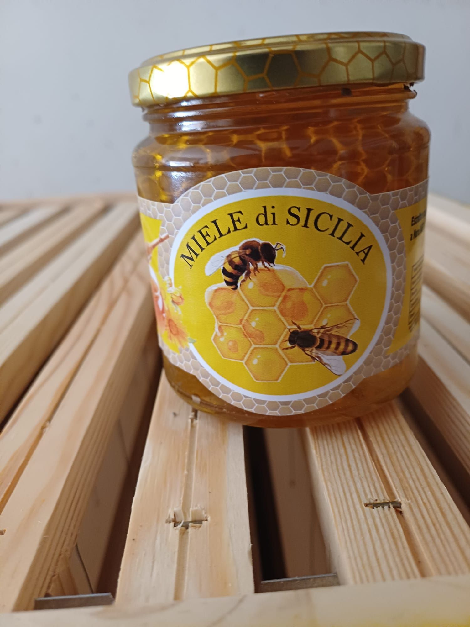 Barattolo di miele siciliano con api e favo su doghe di legno.