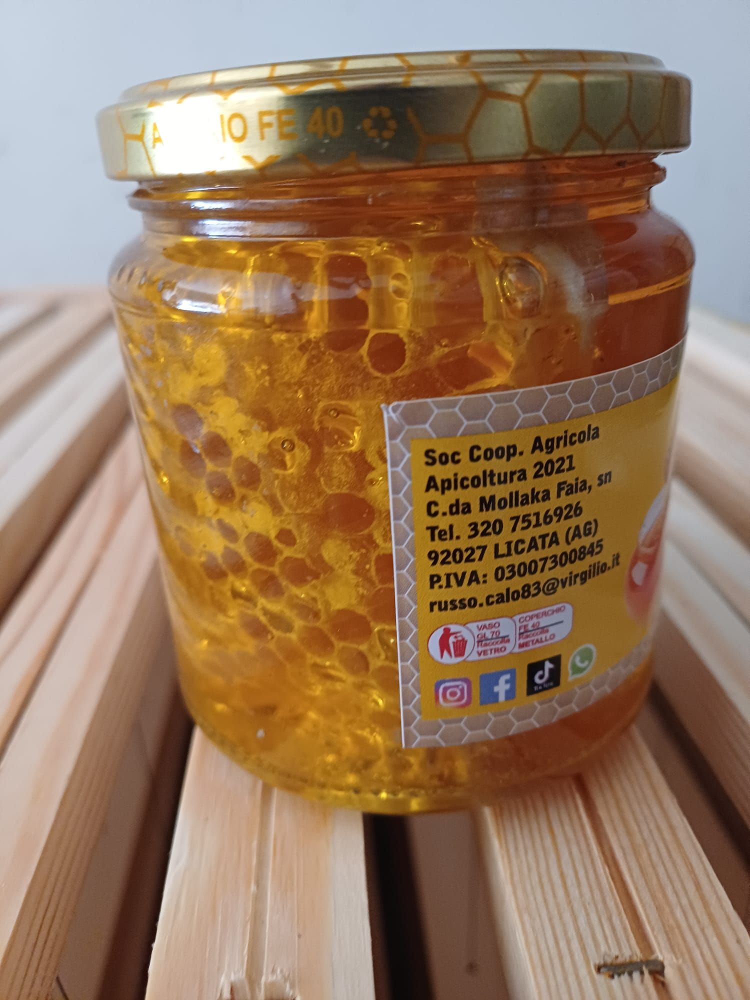 Barattolo di miele con favo su una superficie di legno. Etichetta in italiano.