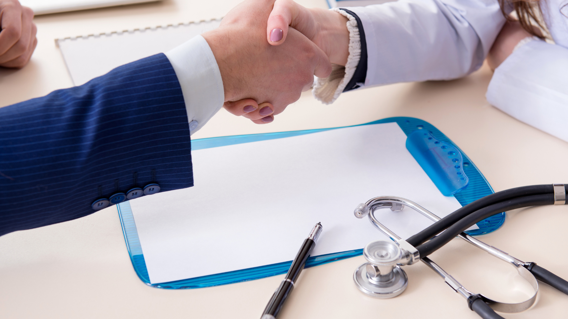 A doctor and a patient are shaking hands over a clipboard.