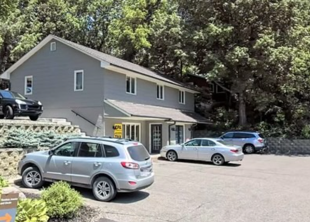 A two-story gray building with several parked cars in a parking lot on a sunny day.