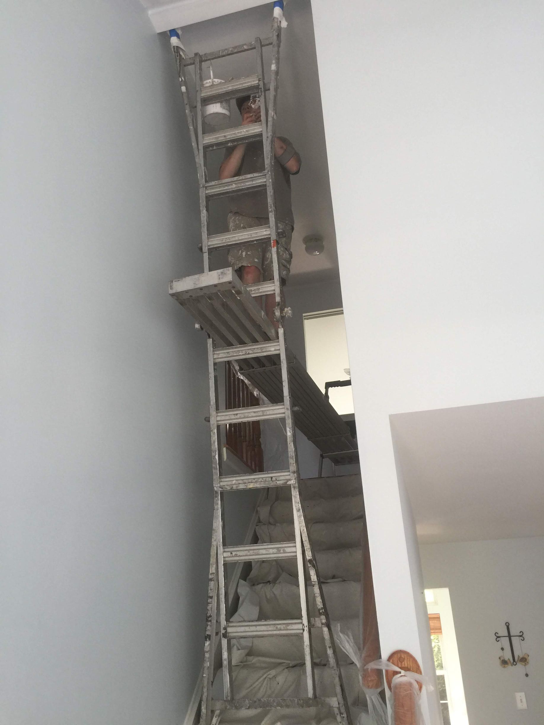 A man is standing on a ladder in a room next to stairs.