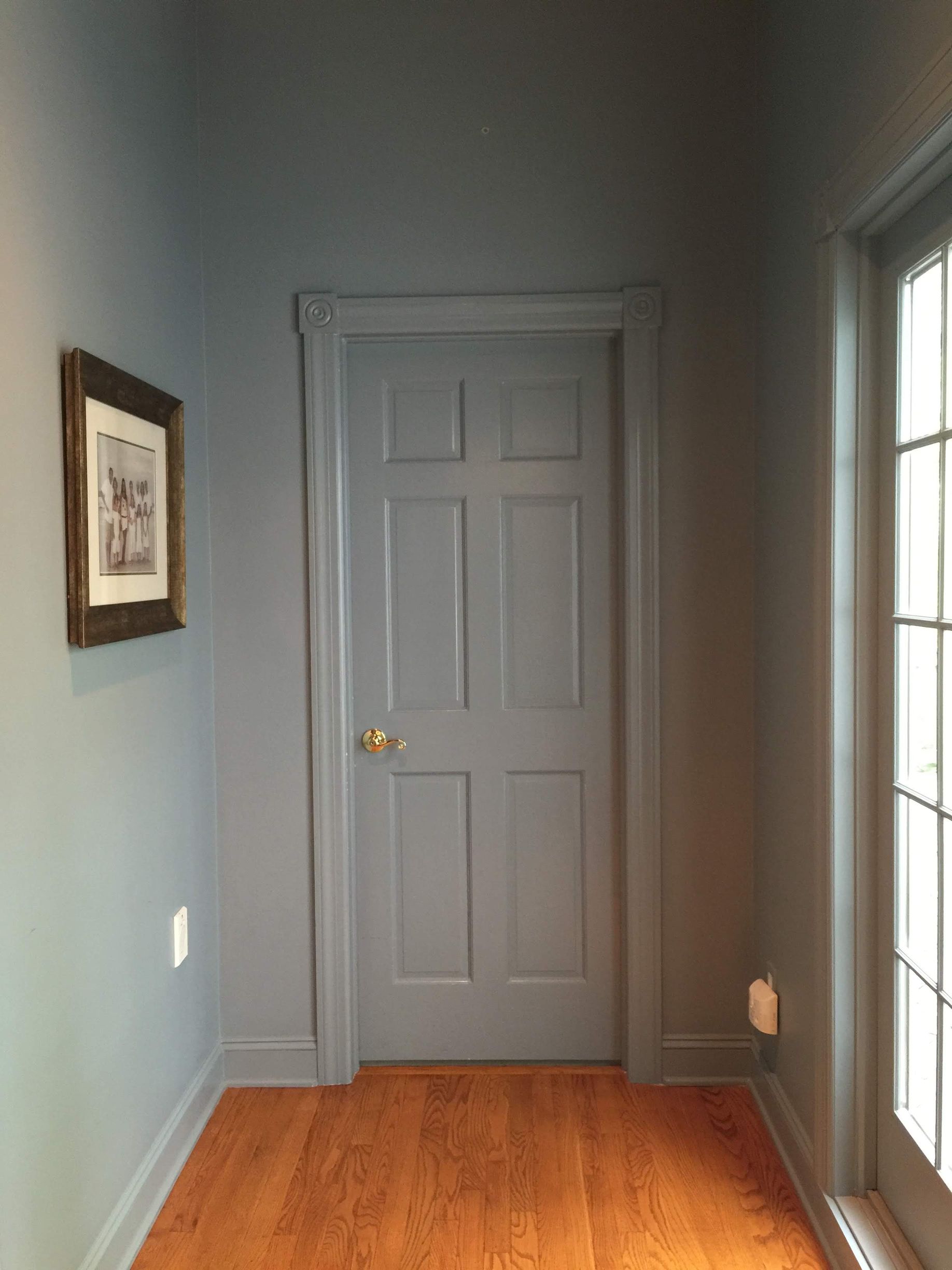 A hallway with a gray door and a picture on the wall.