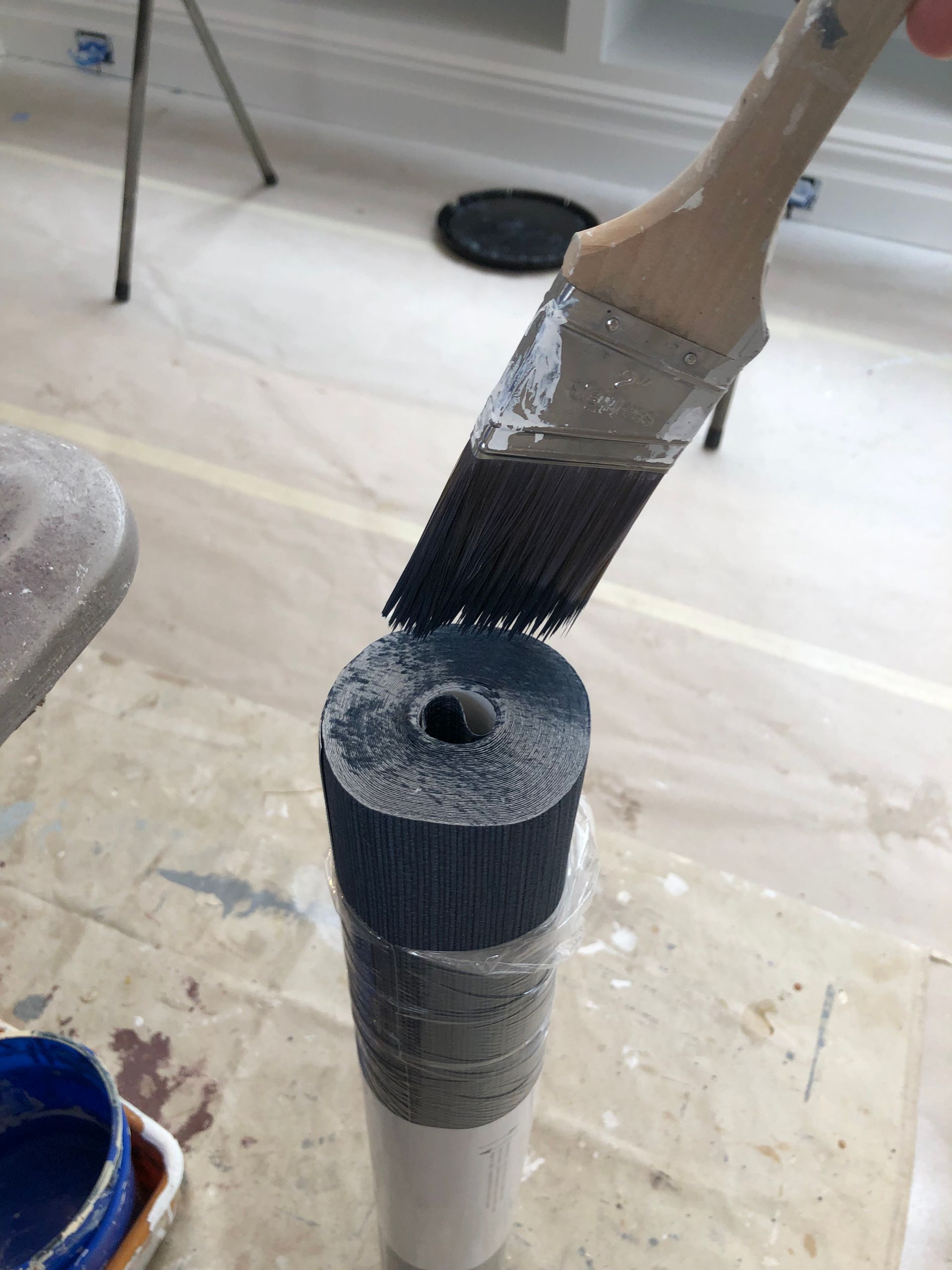 A person is holding a paint brush over a tube of paint.