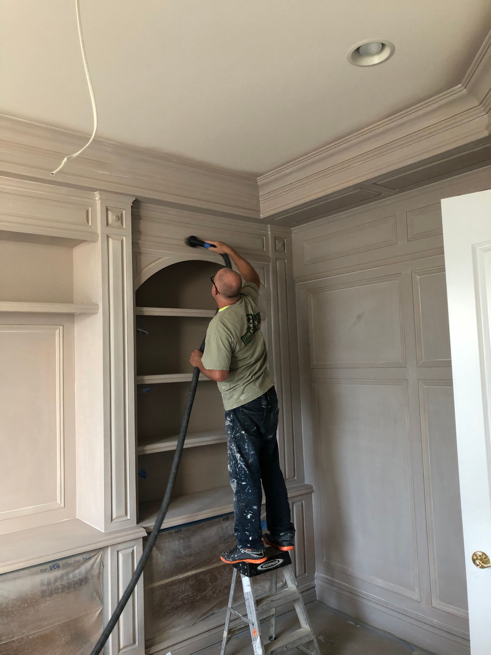 A man is standing on a ladder cleaning shelves in a room.