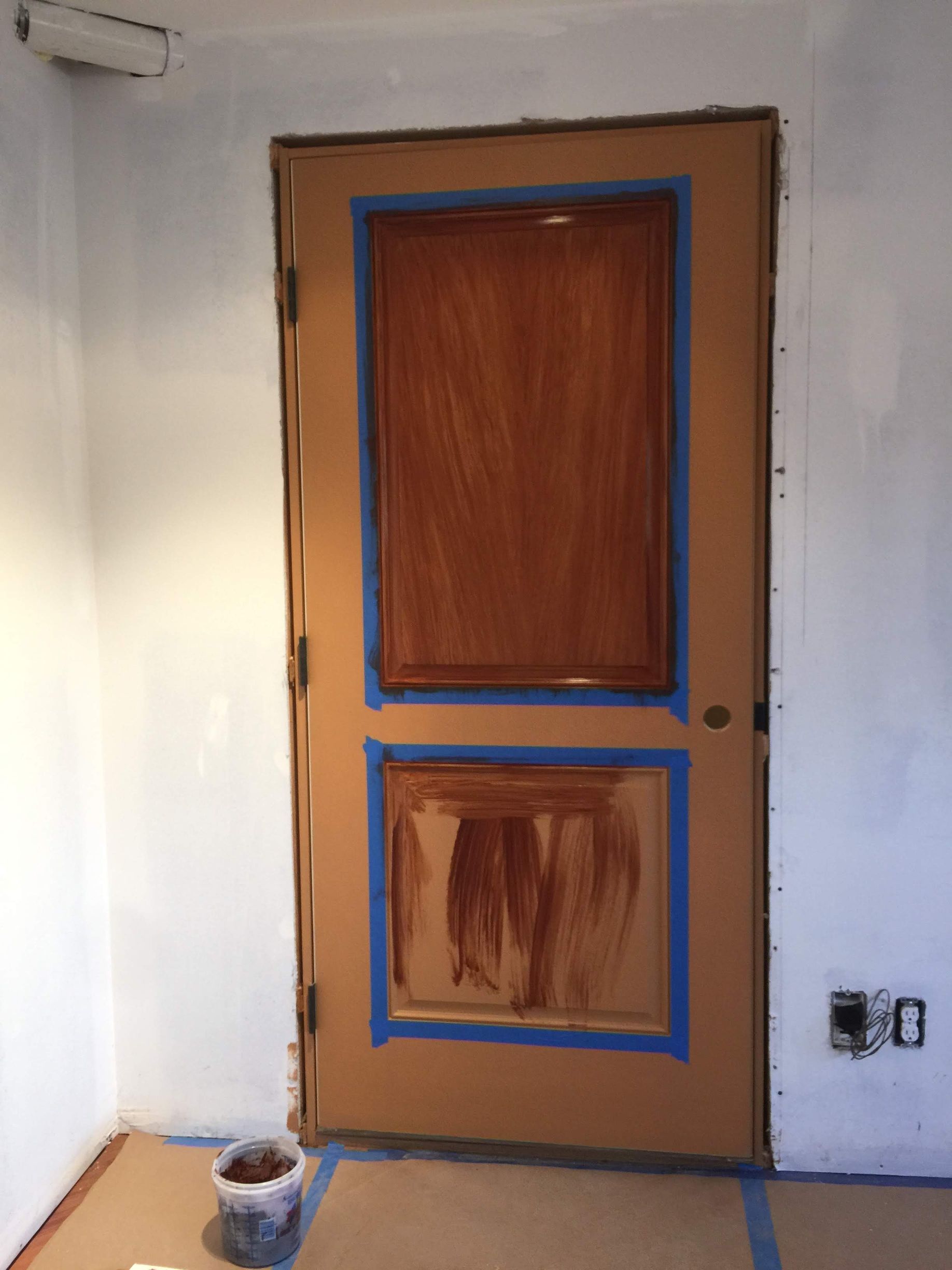 A door is being painted in a room with a bucket of paint on the floor.