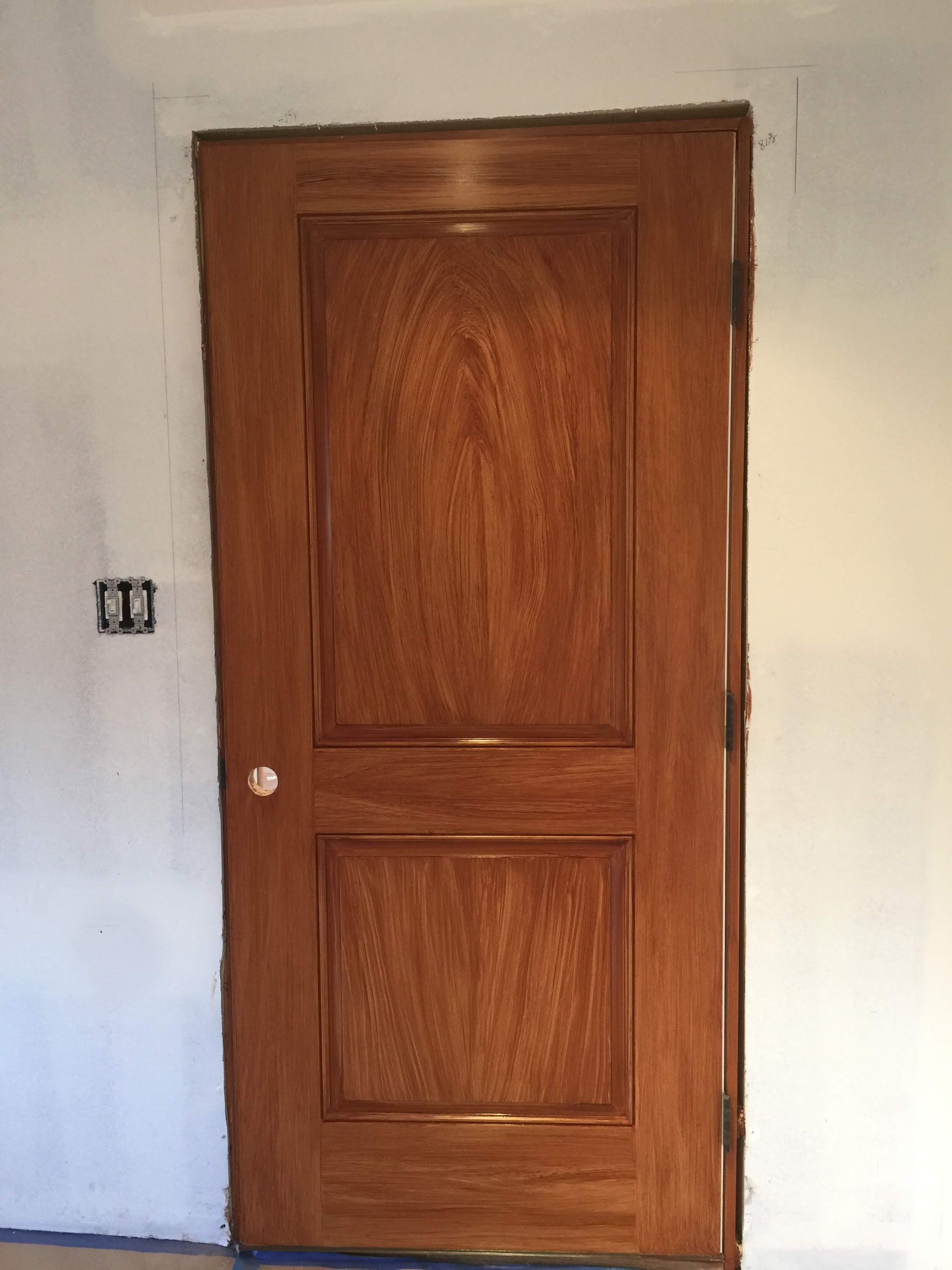 A wooden door is sitting in a room next to a white wall.