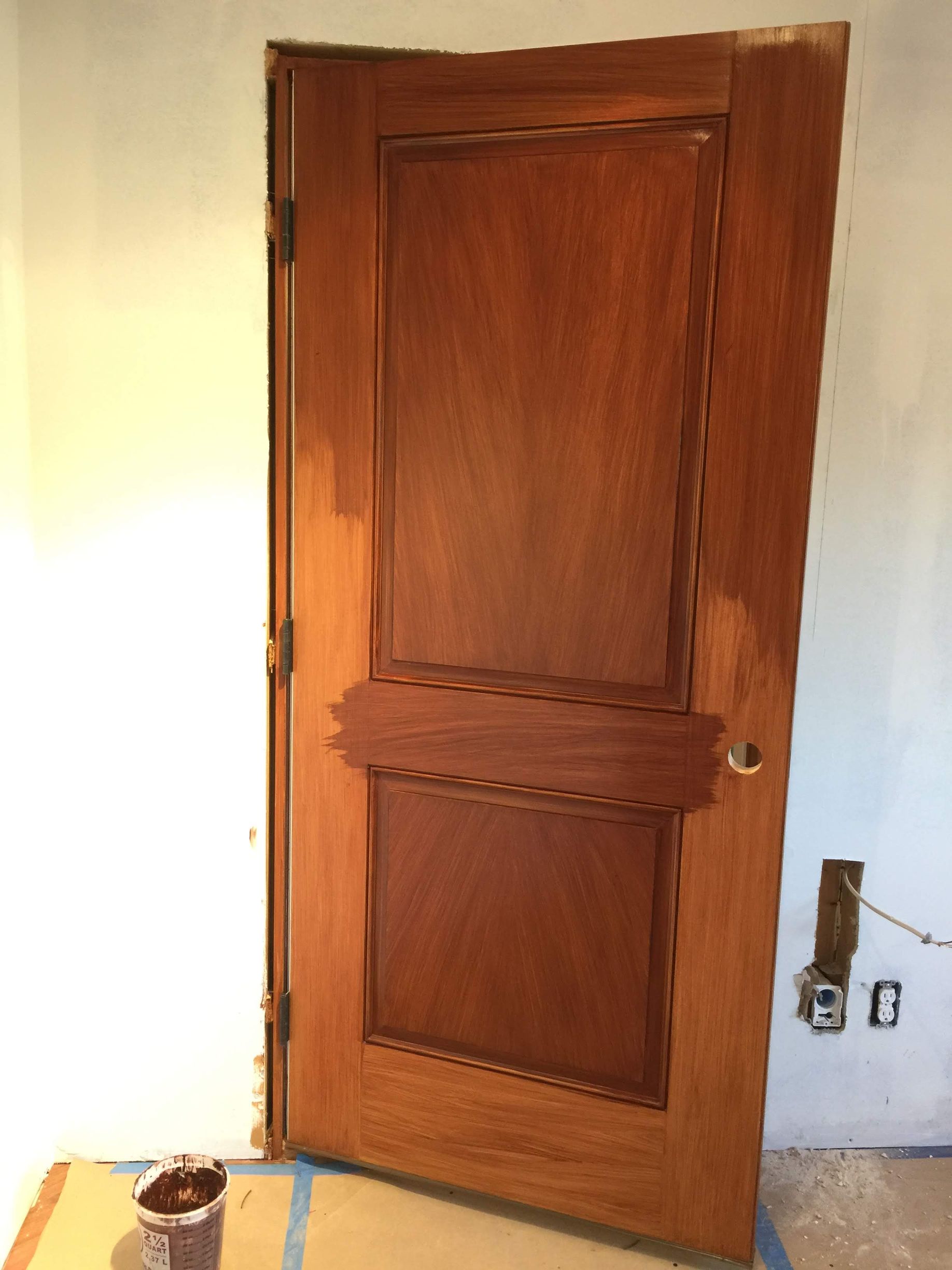 A wooden door is being painted in a room.