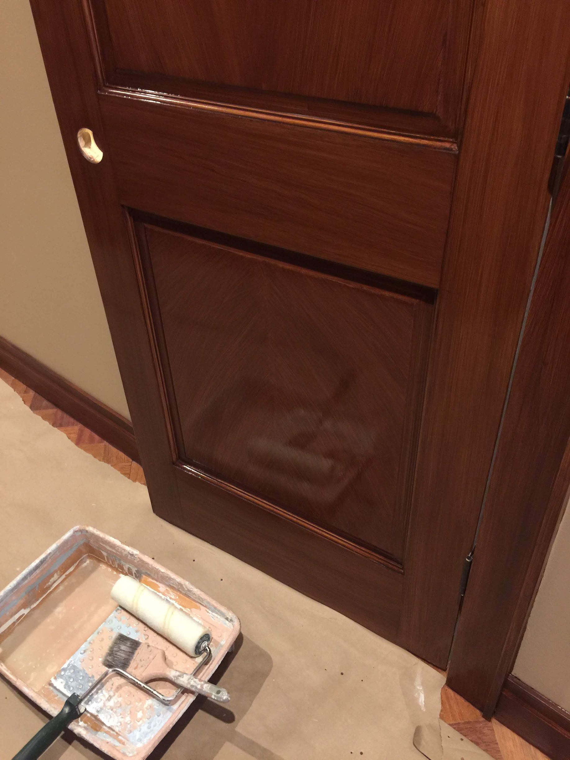 A wooden door is being painted with a tray of paint and a roller