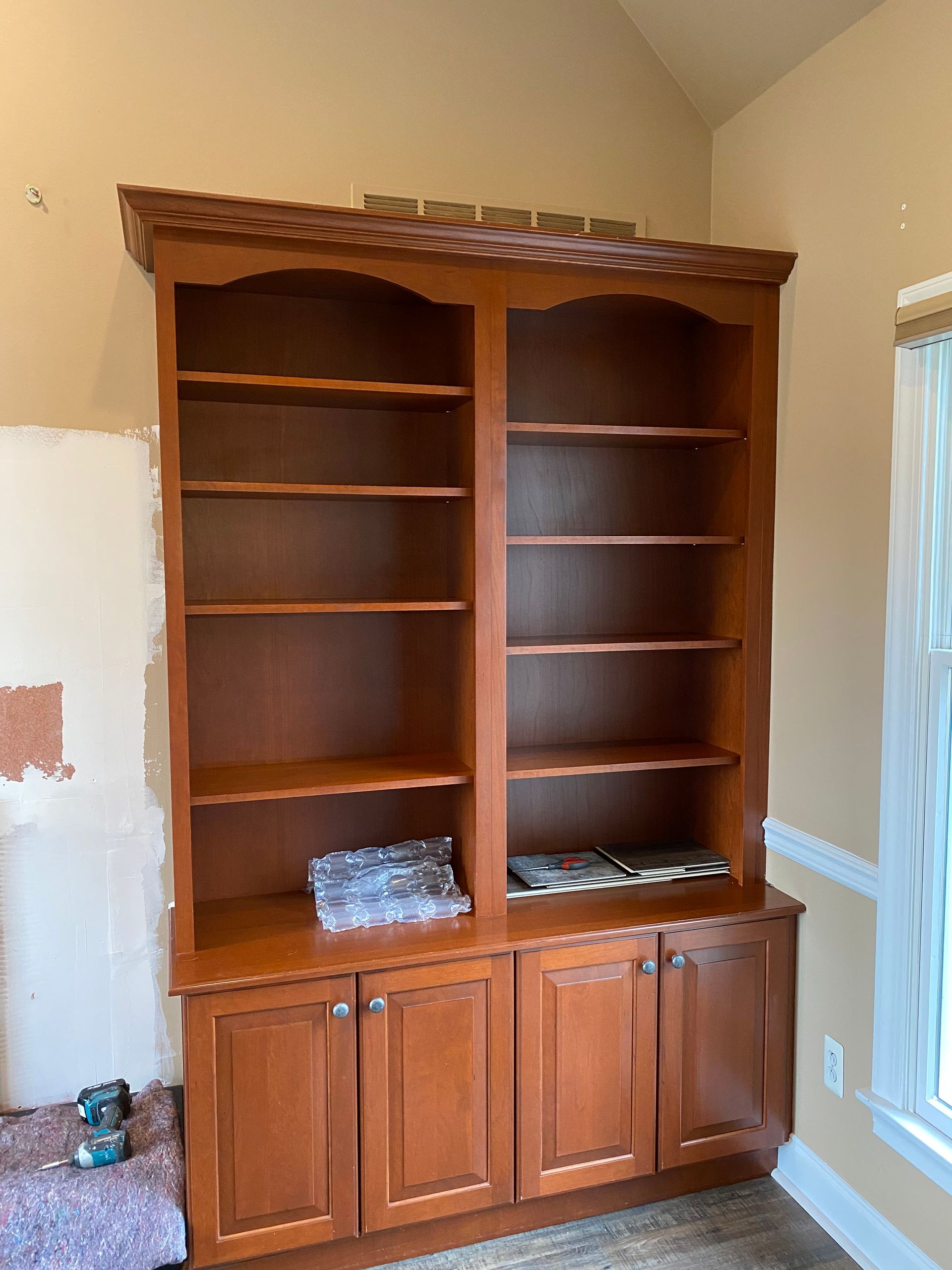 A large wooden bookcase is in a room next to a window.