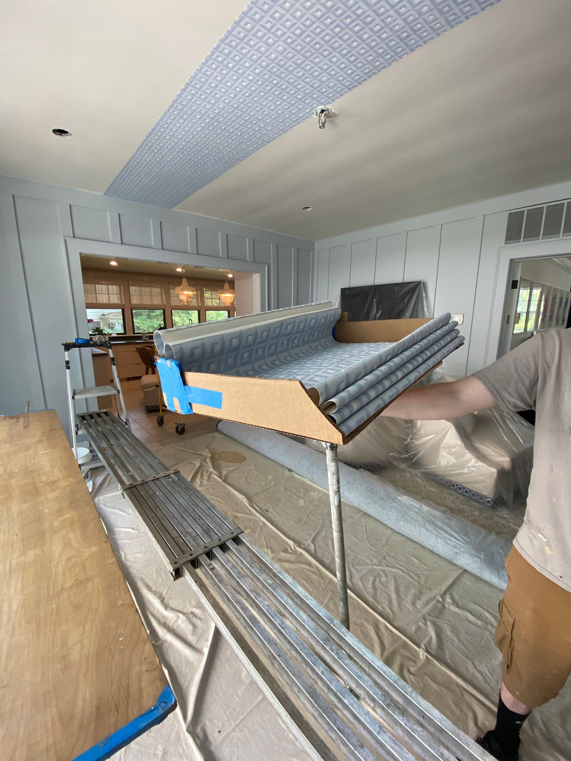 A man is holding a box of carpet in a living room.