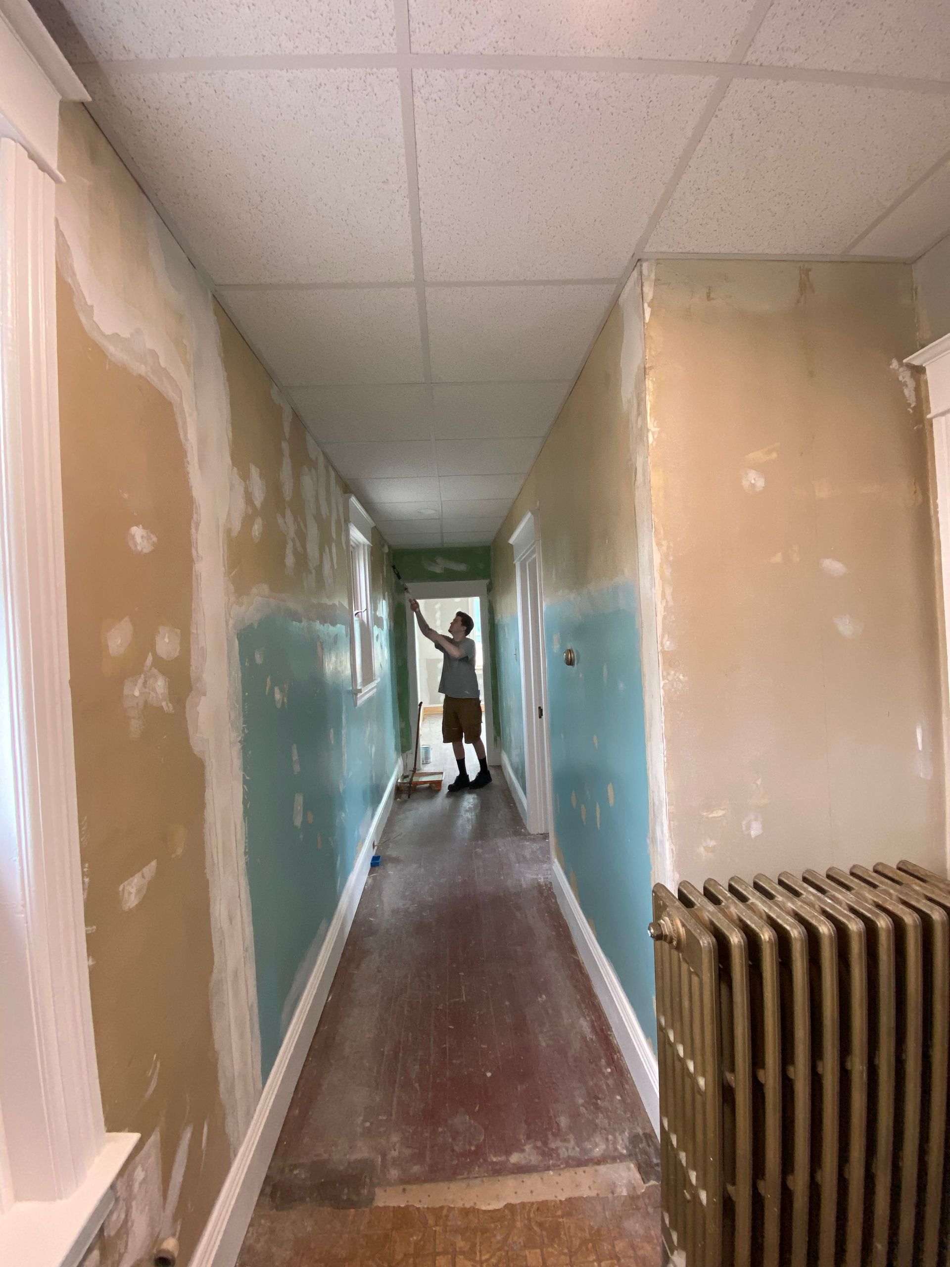 A man is standing in a long hallway with a radiator.