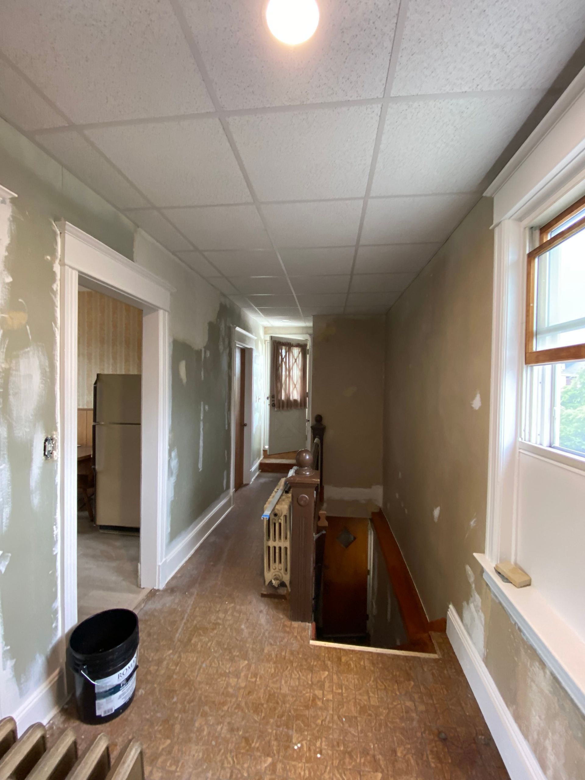 A long hallway in a house with a bucket of paint on the floor.