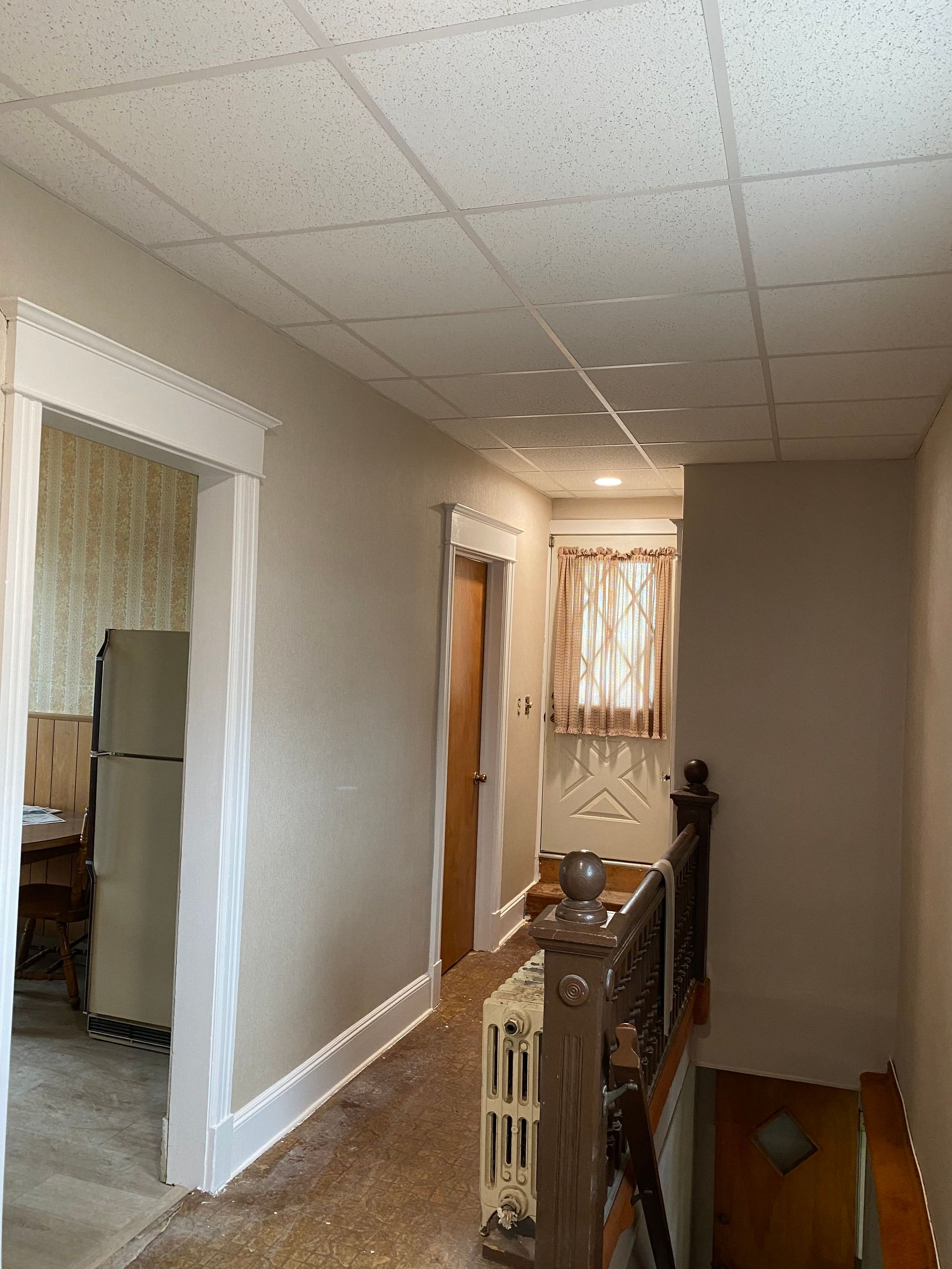 A hallway with a staircase and a refrigerator in a house.