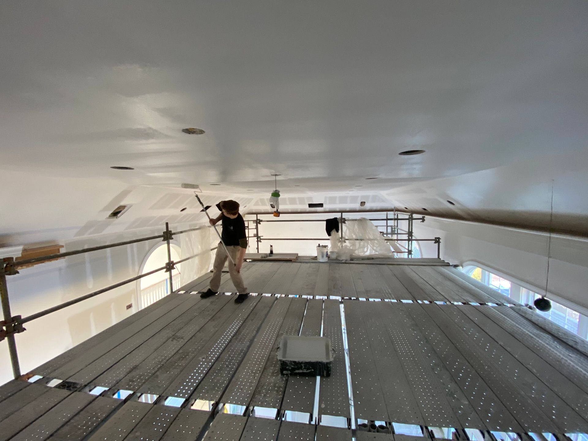 A man is standing on a scaffolding painting the ceiling
