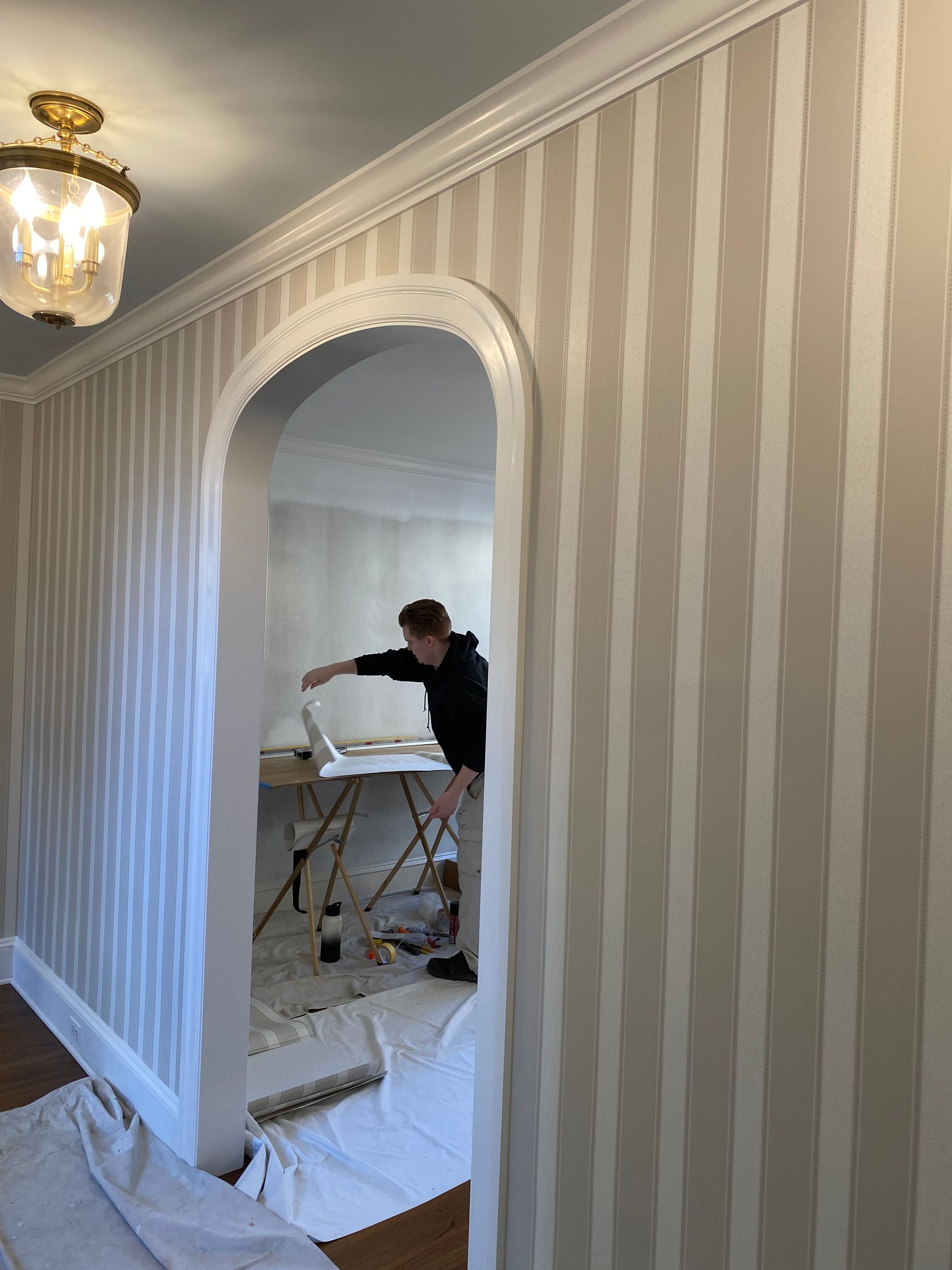A man is standing in a room with striped wallpaper.
