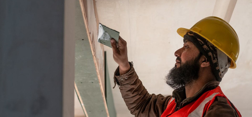 Obrero de la construcción, con casco amarillo y chaleco rojo, aplicando yeso.