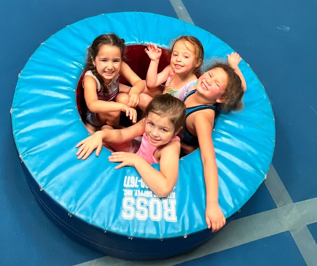 A group of young girls are sitting on a blue ross foam mat