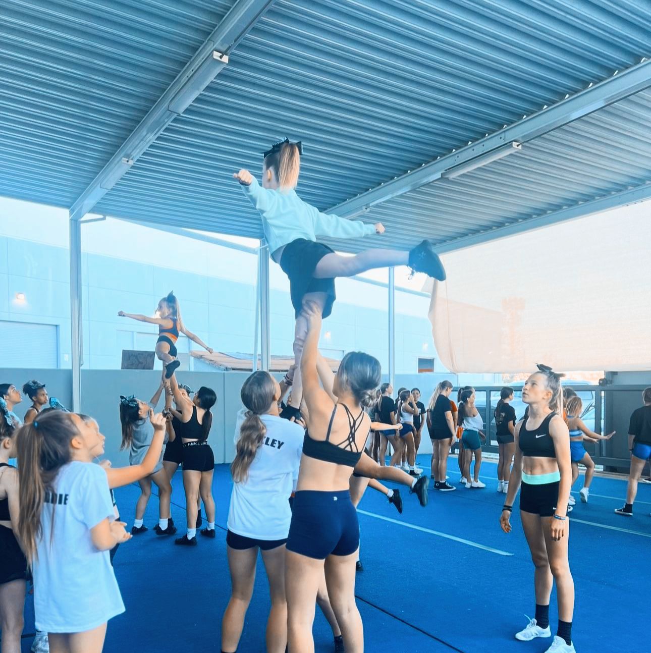 A cheerleader wearing a fly shirt is being lifted in the air