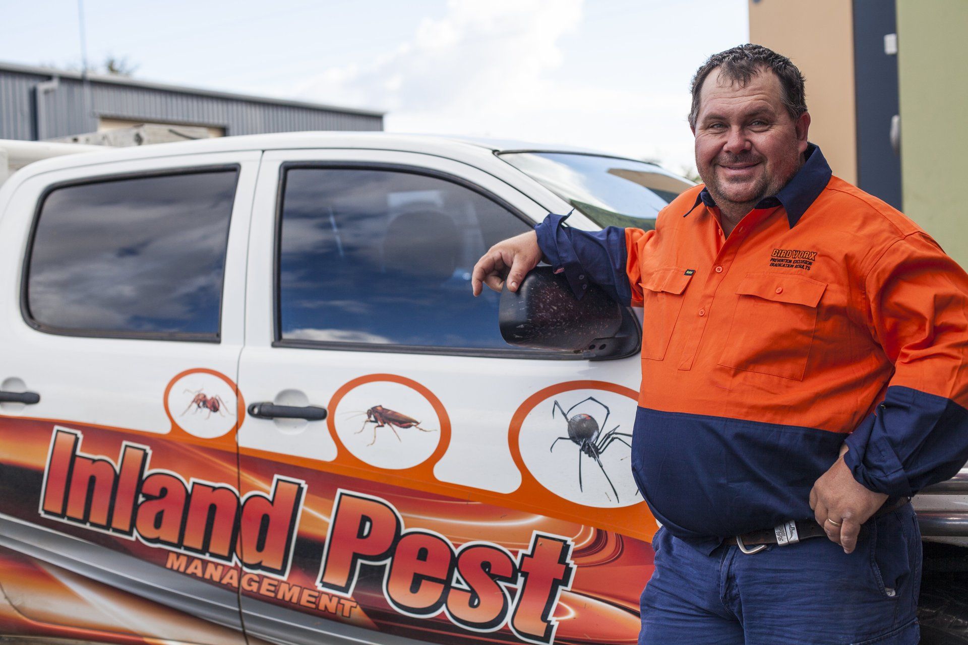 A man is standing in front of a truck that says inland pest management