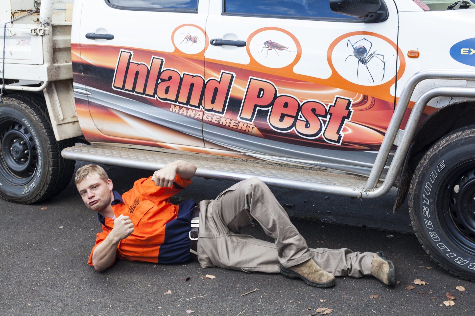 A man is laying on the ground next to a truck that says inland pest