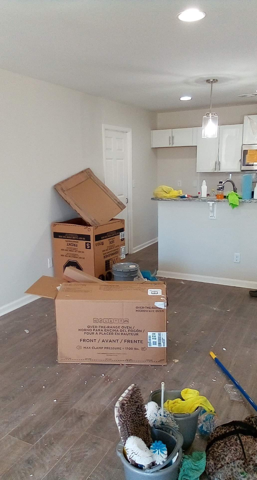 Boxes and cleaning supplies litter a new home's living room and kitchen.