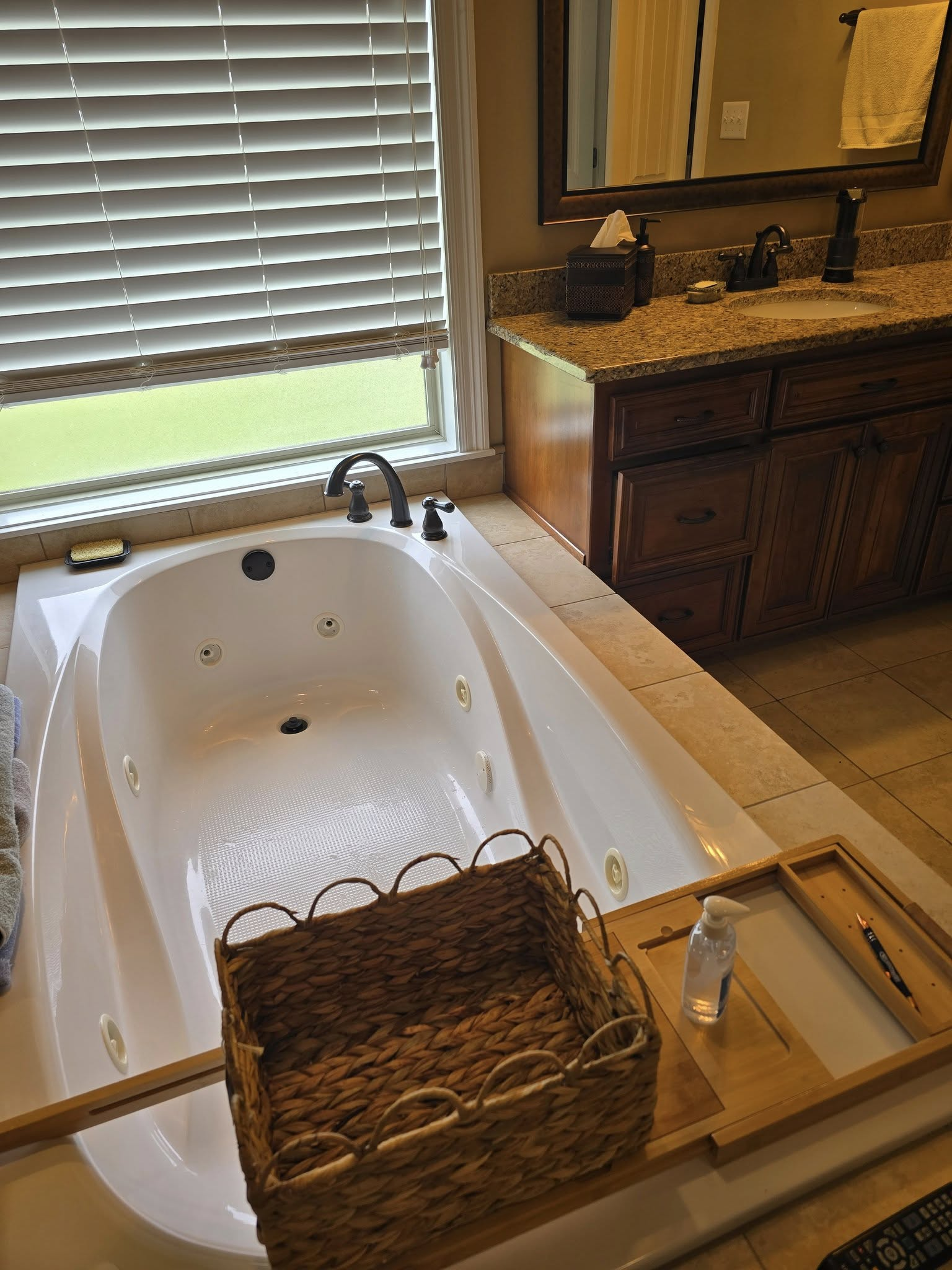 A whirlpool tub with a basket and tray next to a window and vanity.