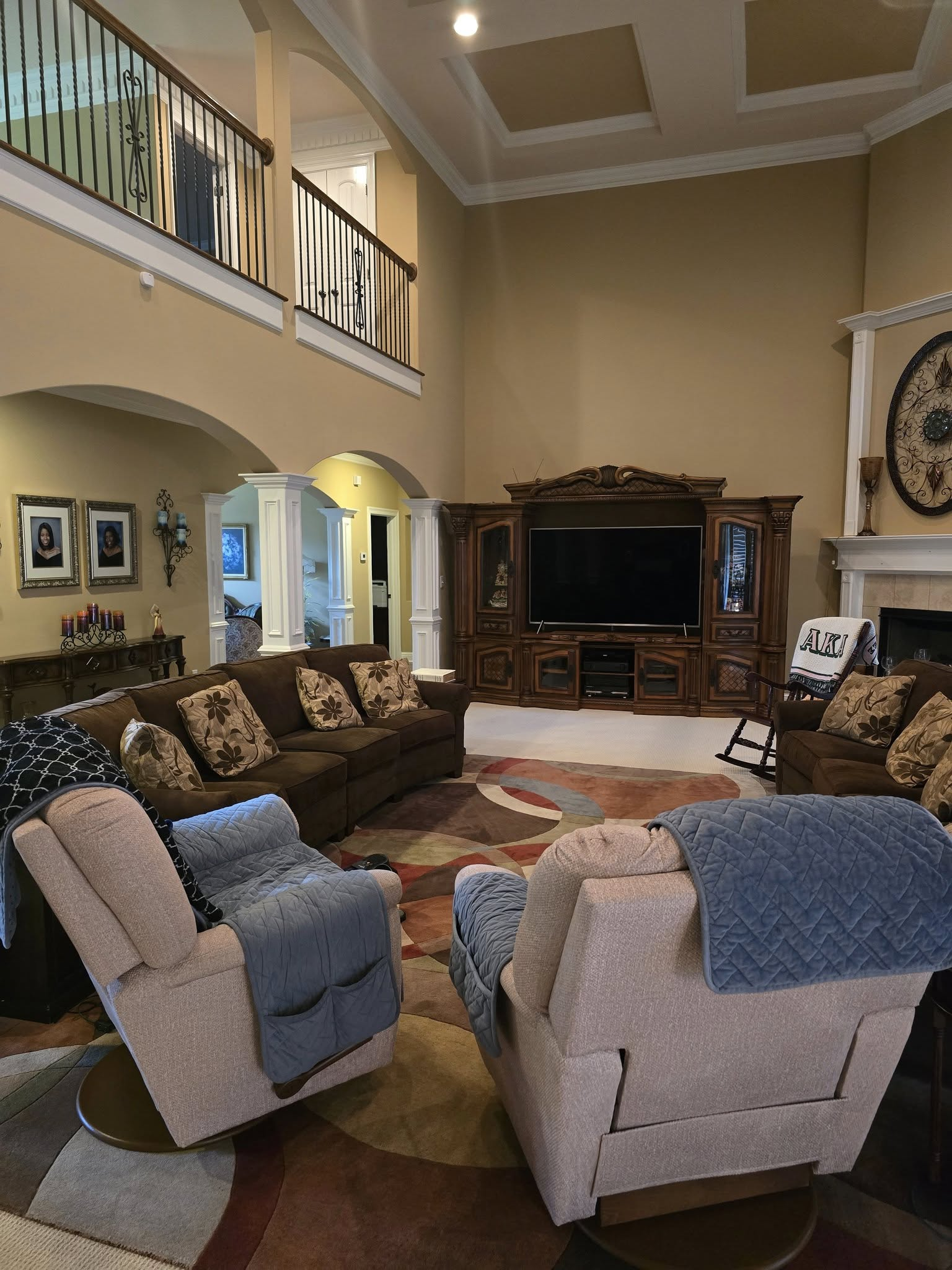 Living room with brown furniture, TV, and high ceiling. Recliners with blue blankets face the sofa.