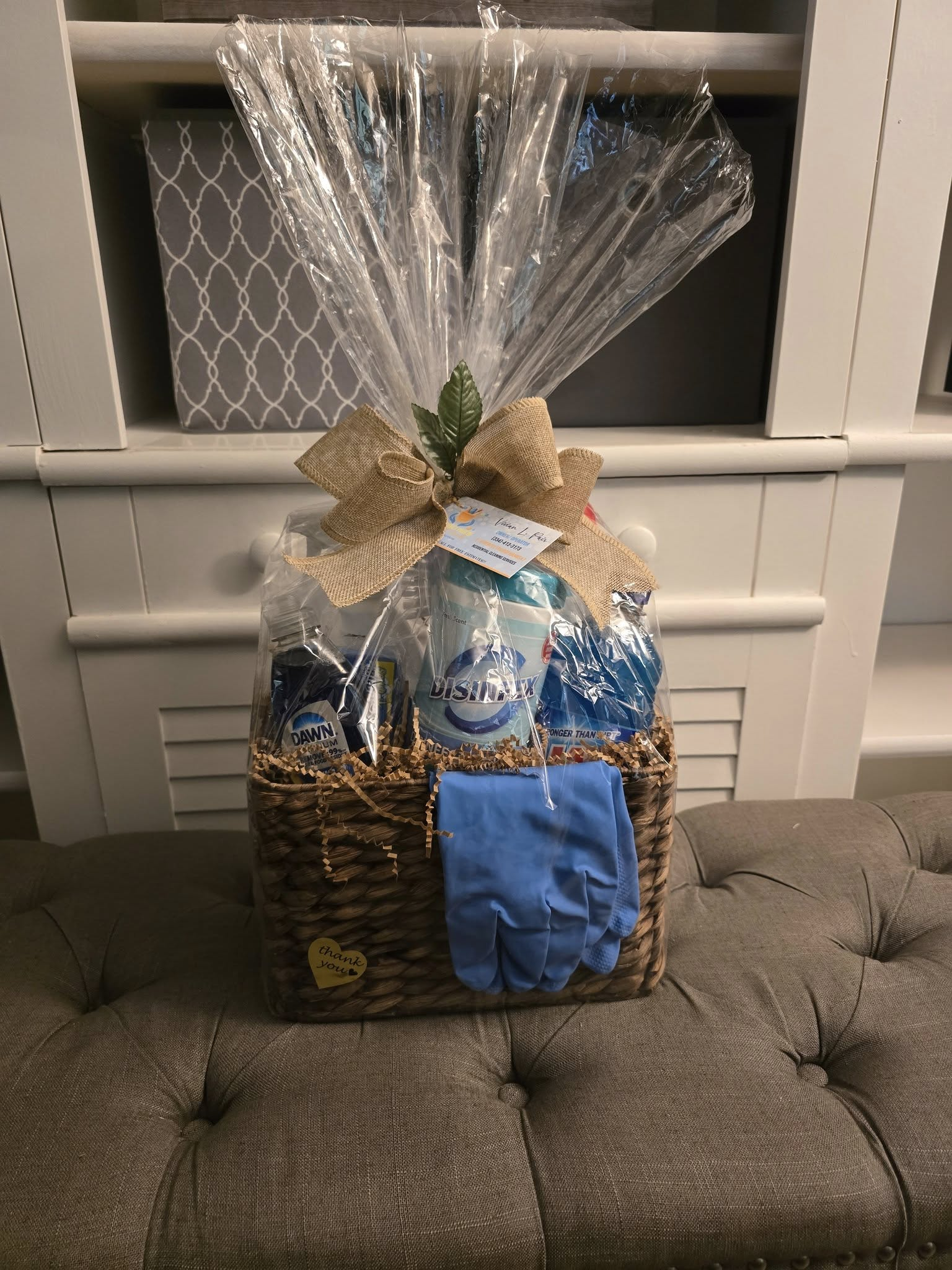 Gift basket with cleaning supplies, wrapped with clear cellophane and a burlap bow.