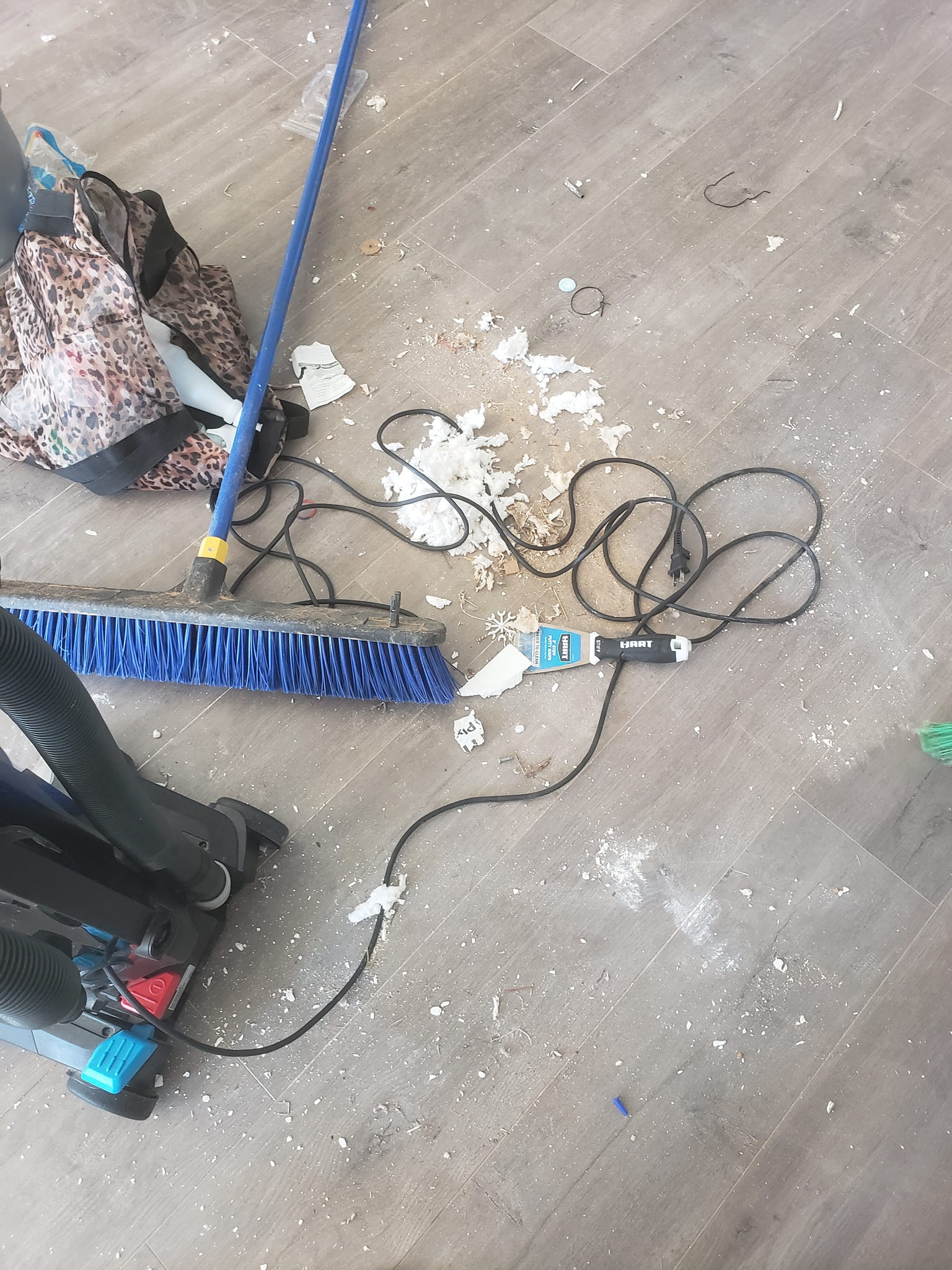 Messy floor: debris, broom, black shoes, bag, and a charging cable.