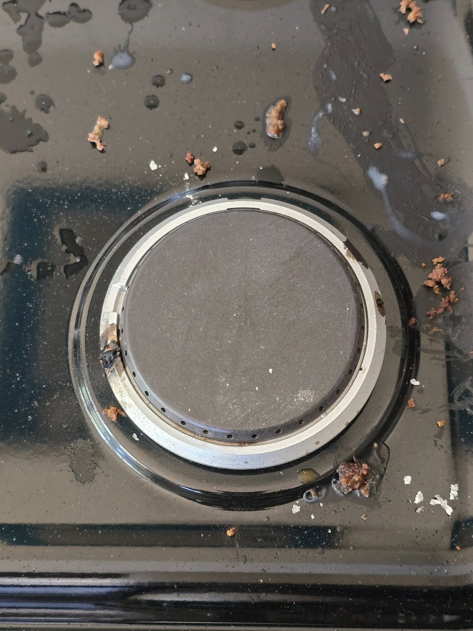 Dirty stovetop burner with food debris and spills.