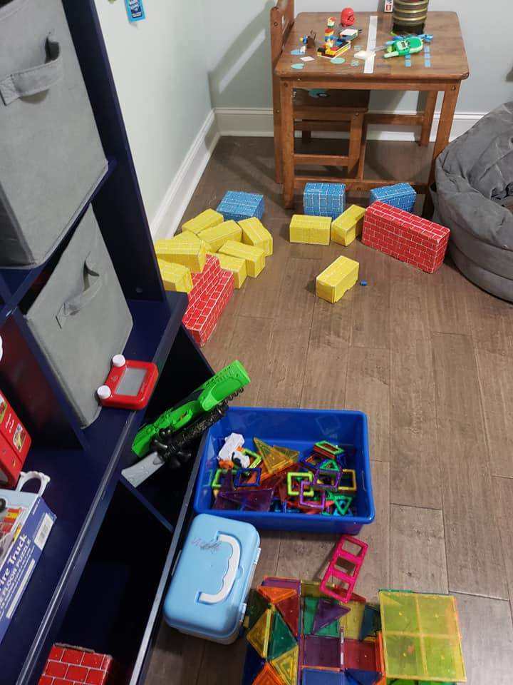 Playroom with scattered toys, wooden floor, and a small table with toys.