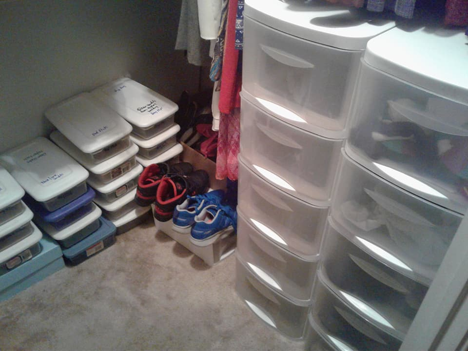 Closet with stacks of white storage containers, shoe racks, and plastic drawers.