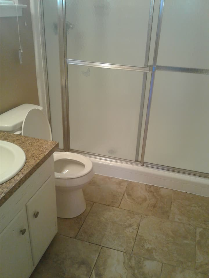Bathroom with a toilet, vanity, and a shower with frosted glass doors. Beige tile flooring.
