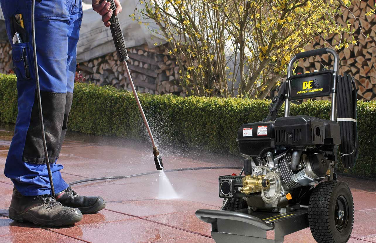 Person power washing a brick patio with a gas-powered pressure washer outside.