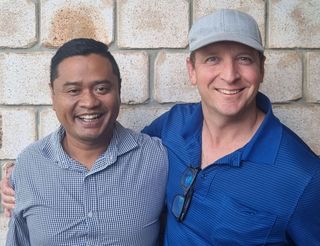 Two men are posing for a picture in front of a brick wall.