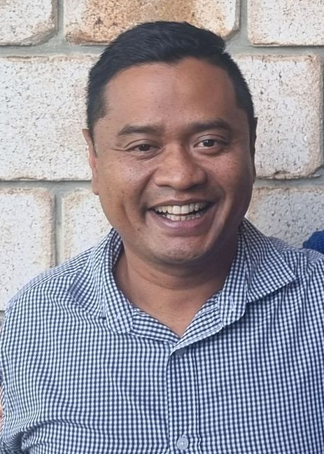 Two men are posing for a picture in front of a brick wall.