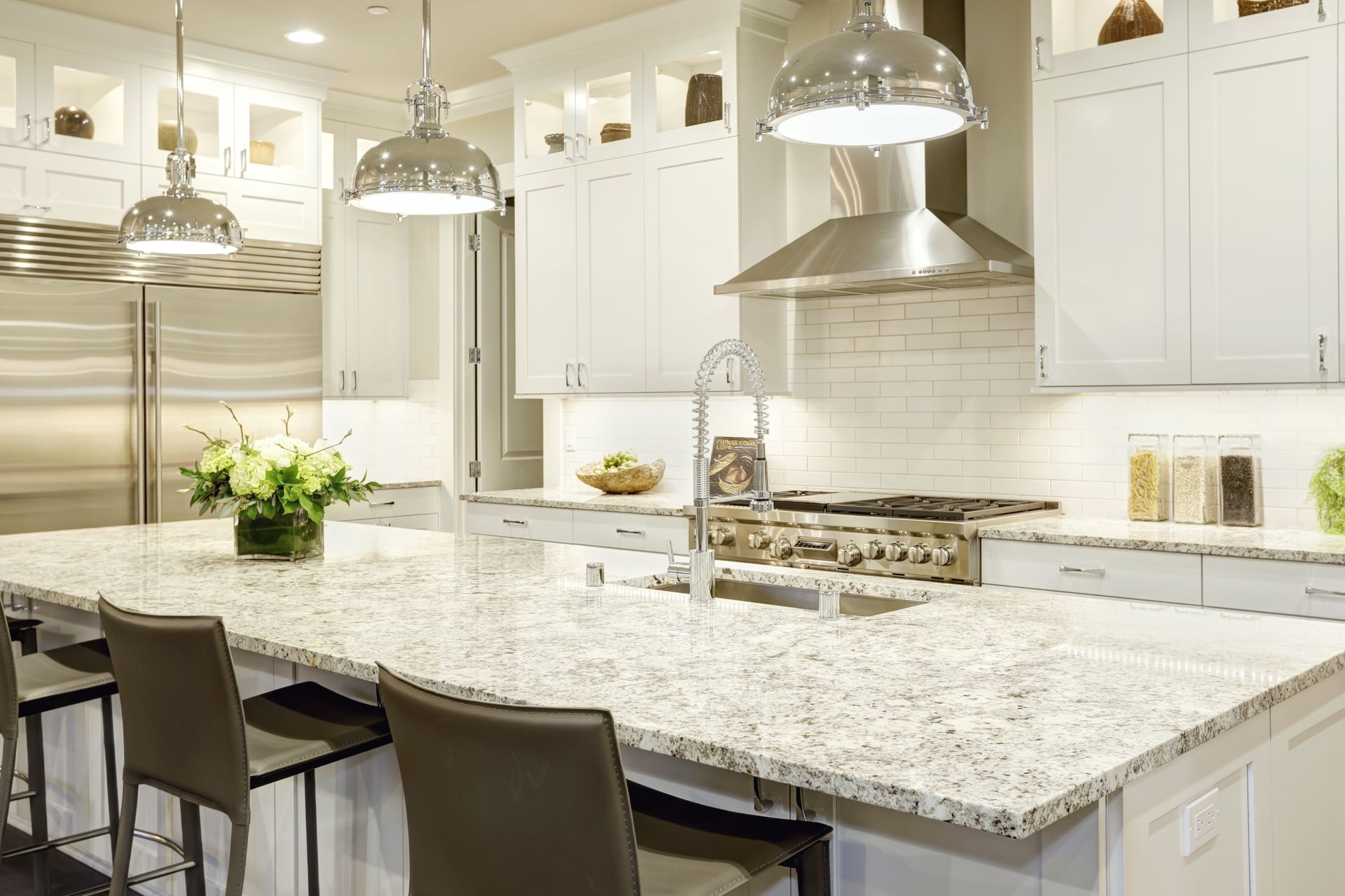 Modern kitchen with granite island, pendant lights, and stainless steel appliances.