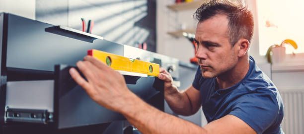 Person using a spirit level to align black cabinet during home improvement or furniture installation.