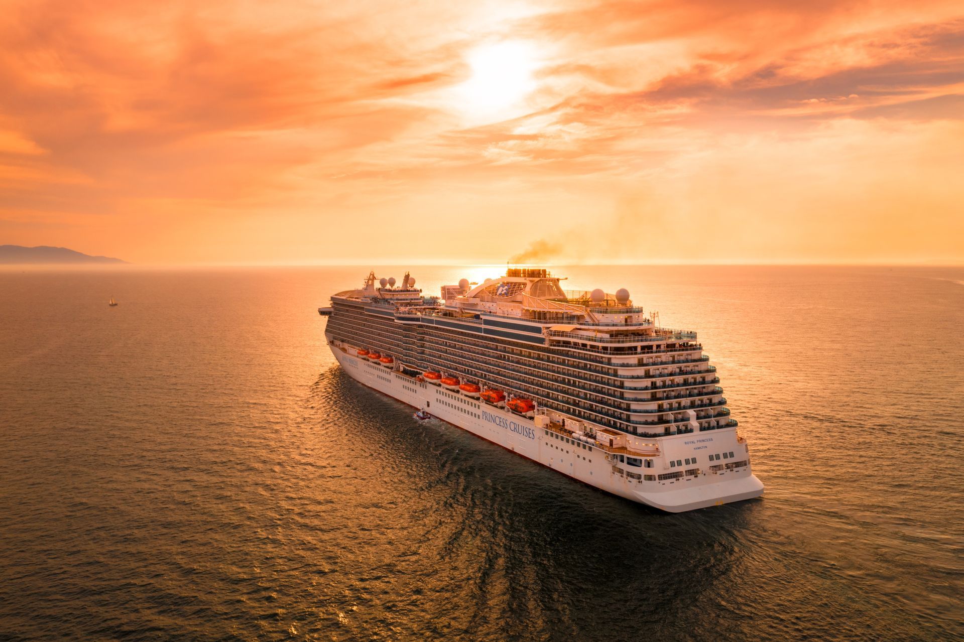 Cruise ship sailing on calm water at sunset. Orange and golden sky.