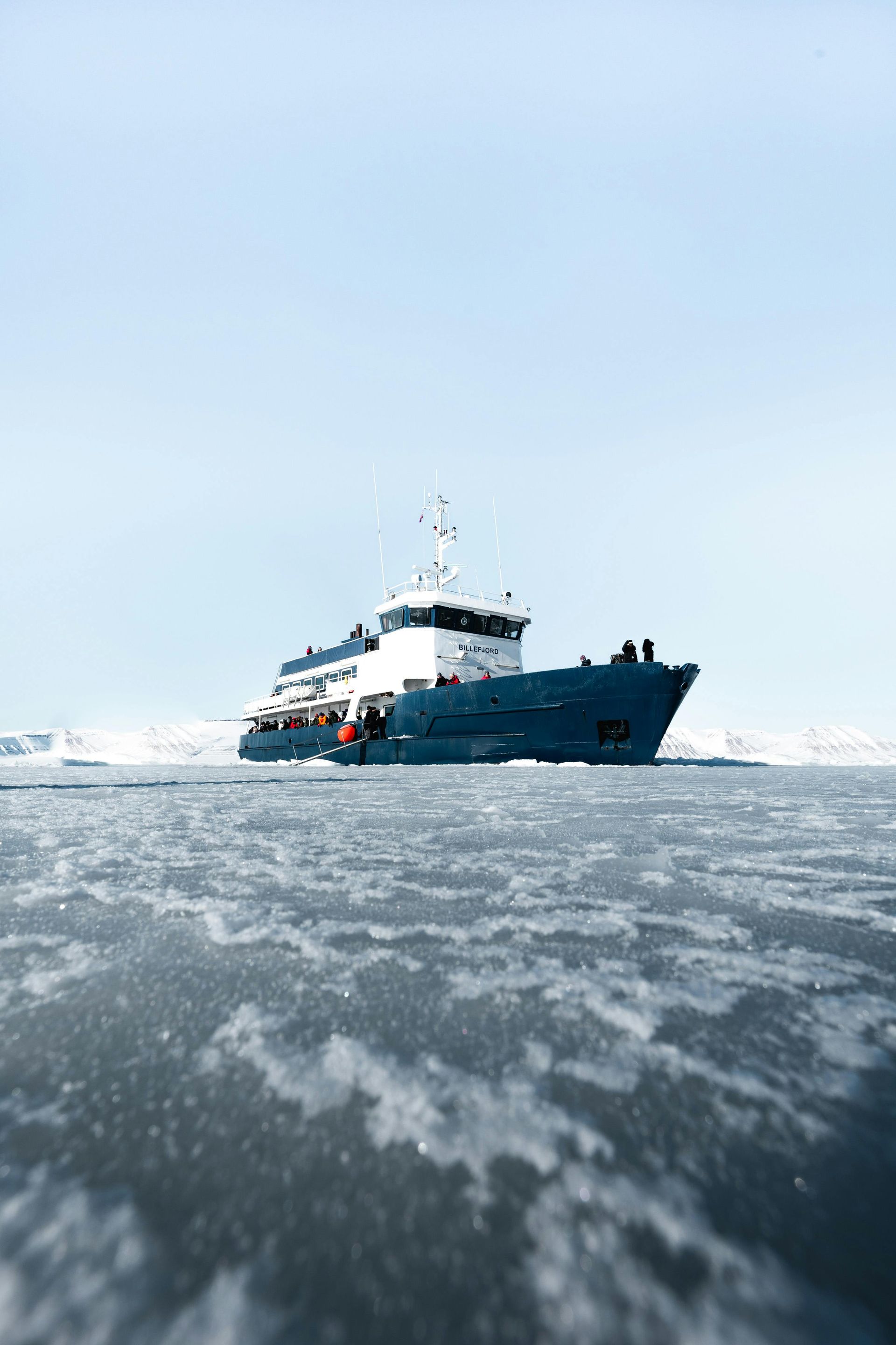 Blue ship sailing through icy water, blue sky background.