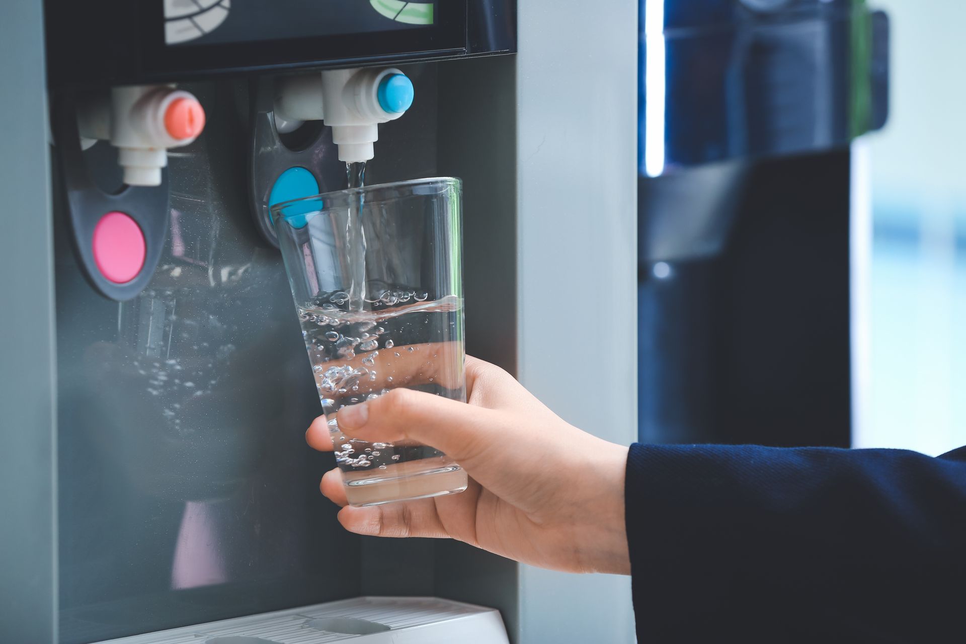 A woman is pouring water from a cooler into a glass.