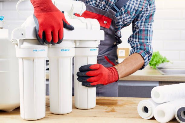 Person in red gloves installing water filter cartridges in a kitchen.