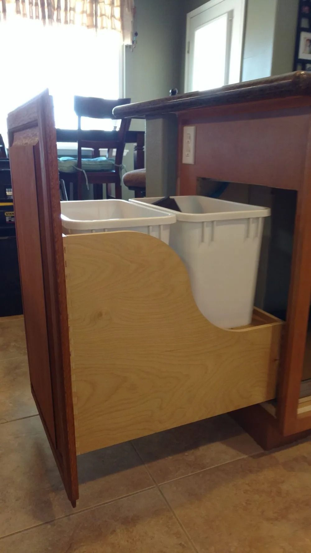 A kitchen cabinet with two trash cans in it.