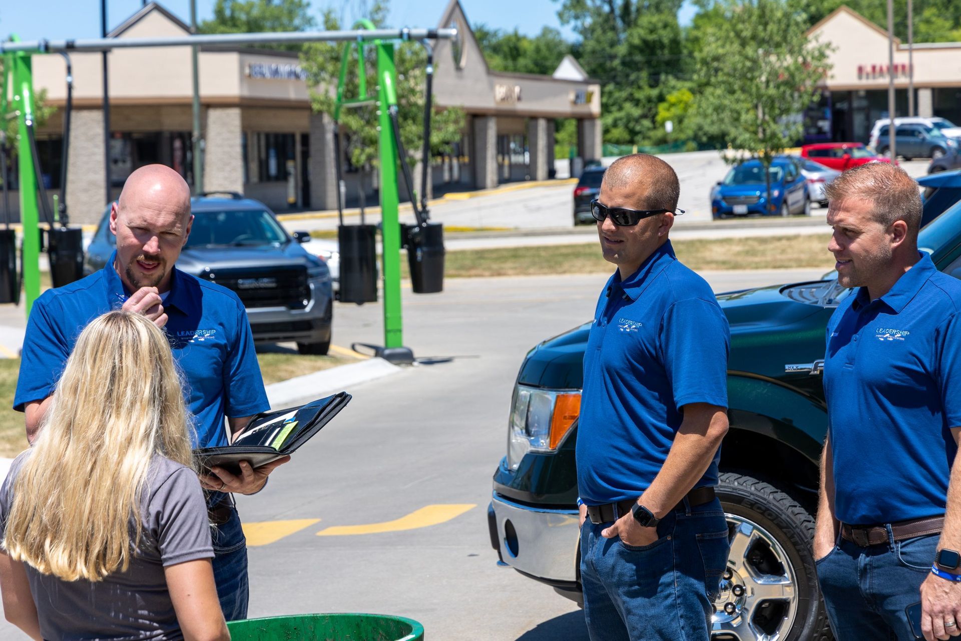 A group of men are standing next to each other in a parking lot talking to a woman.