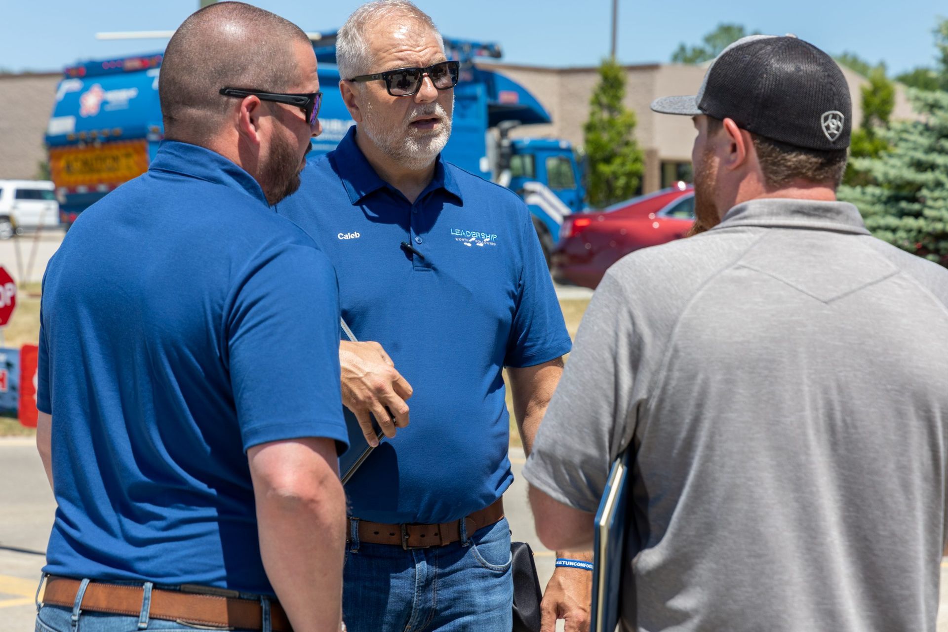 Three men are standing next to each other in a parking lot talking.
