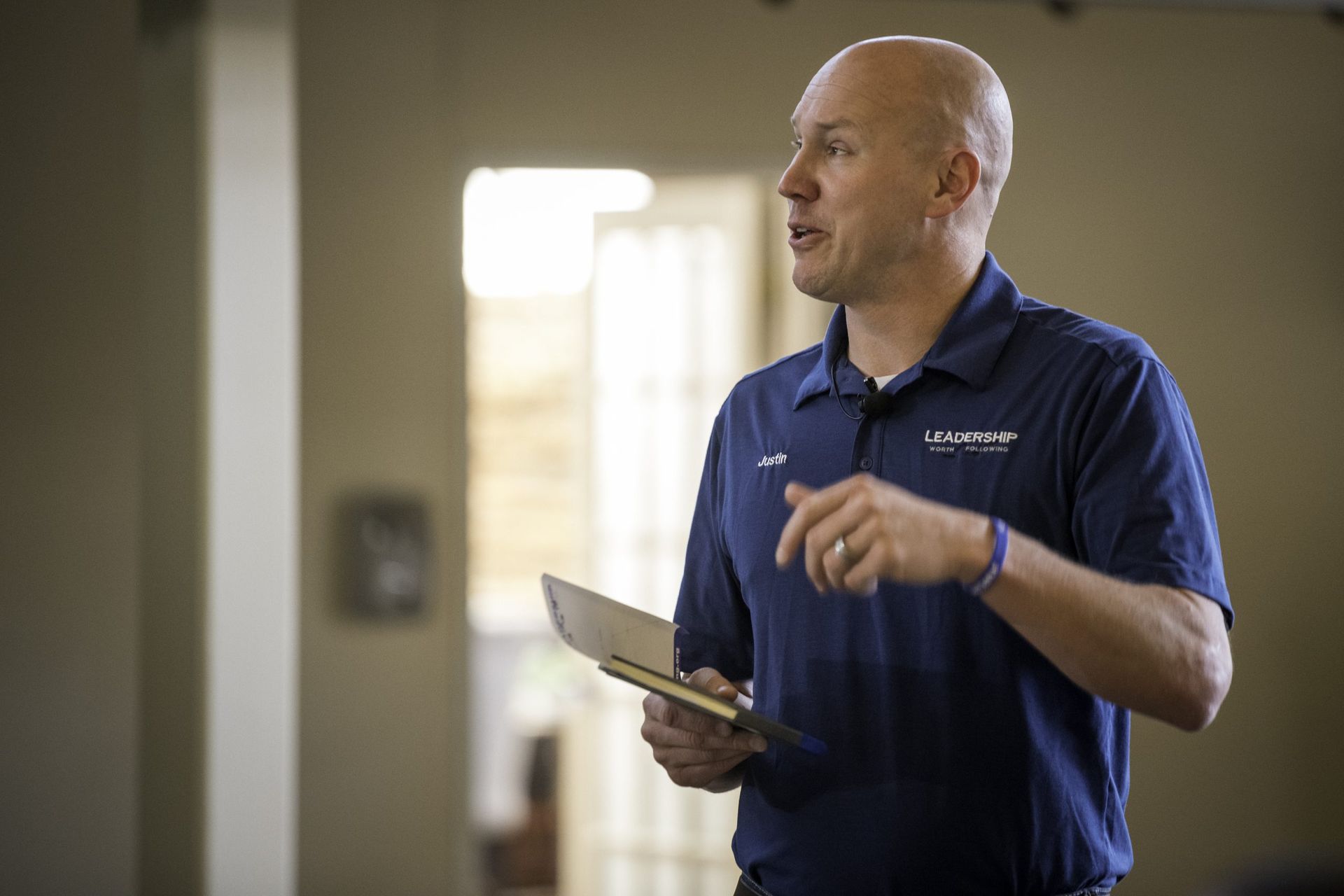 A man in a blue shirt is standing in a room holding a clipboard.